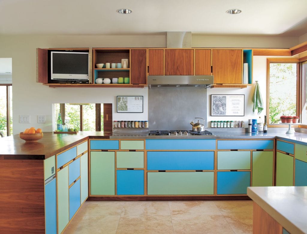 A modern kitchen features colorful laminate cabinets in blue and green, with wood accents.